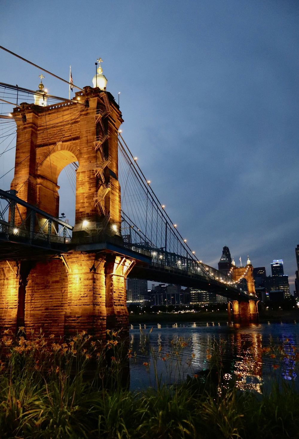 The Roebling Suspension Bridge lit at dusk, with the Cincinnati skyline behind it